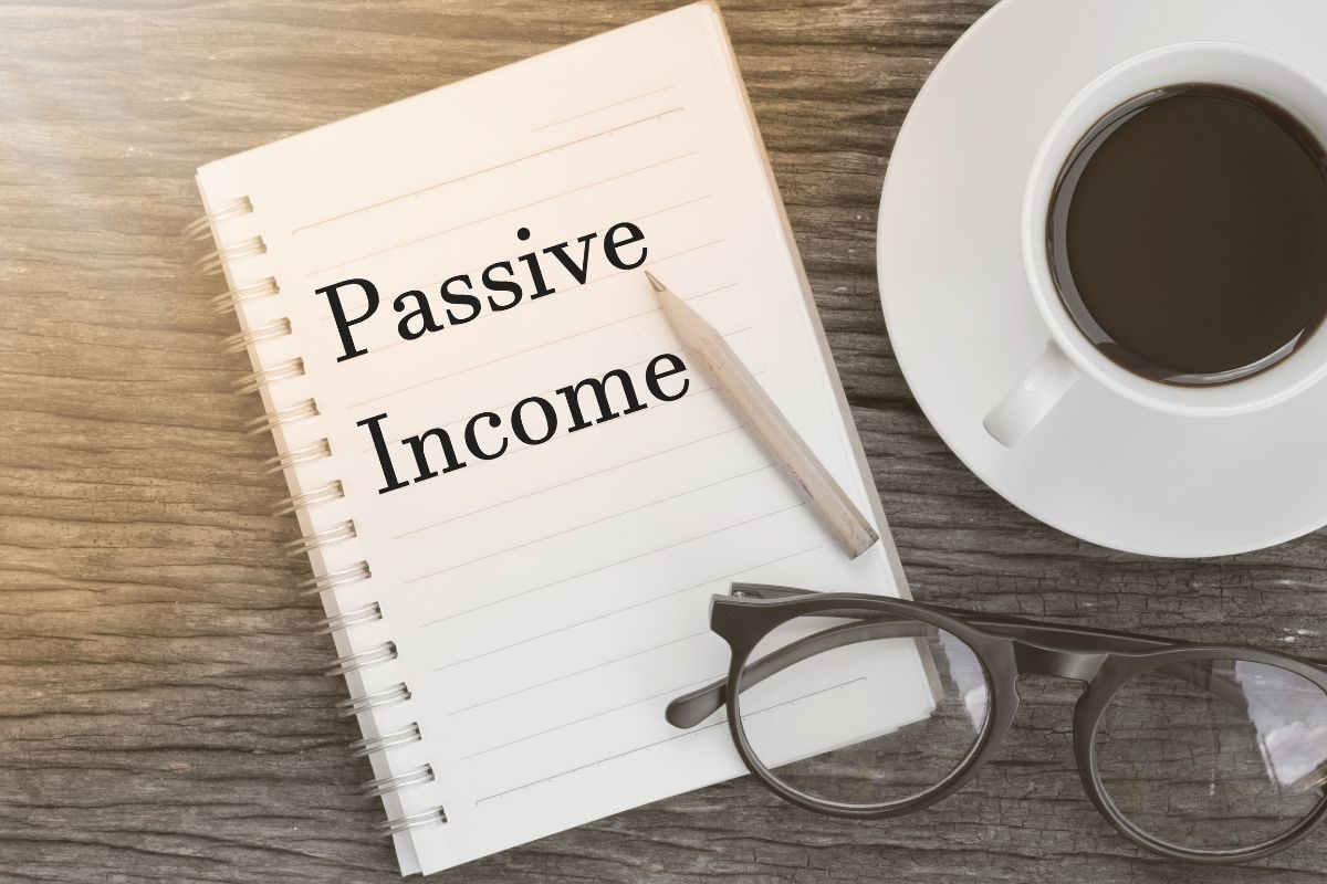 The image shows a coffee, an eyeglass, a pen, and a notebook with notes referring to thinking in terms of scalability and passive income, which is how real wealth is built.