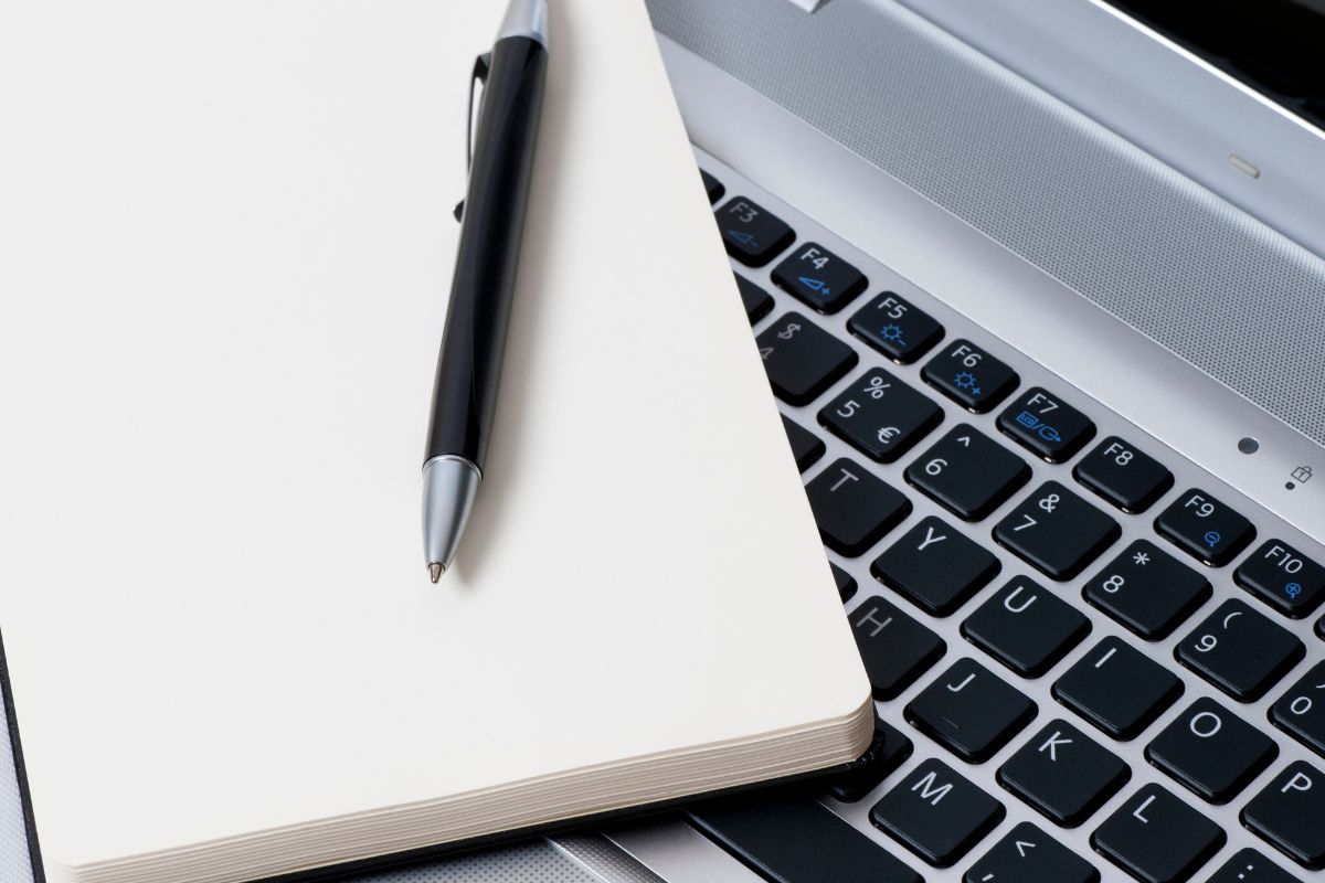 The photo shows a laptop and a notebook with a pen.