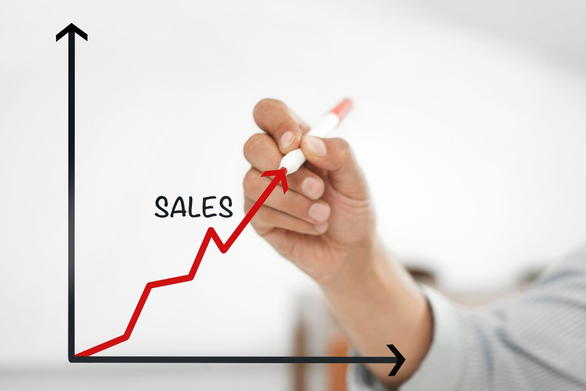 The image shows a man's hand holding a marker and creating a graph and an arrow with a note which means developing high-income skills like sales to increase the earning power and more money you can make.