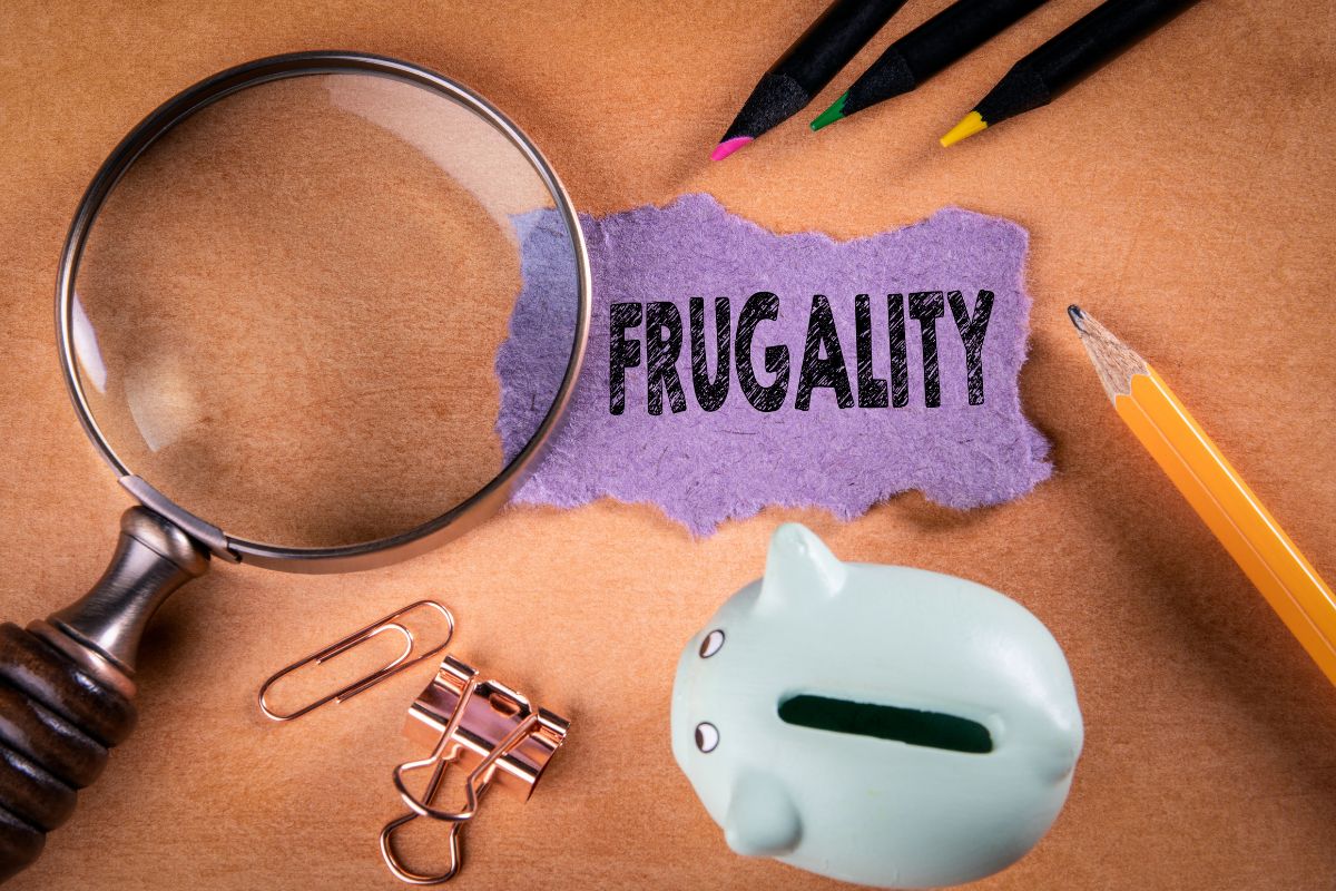 The picture shows colored pens, a piggy bank, a magnifying glass, and a piece of paper with a note indicating to maintain a frugal lifestyle even as wealth increases, and staying smart with money keeps you rich.