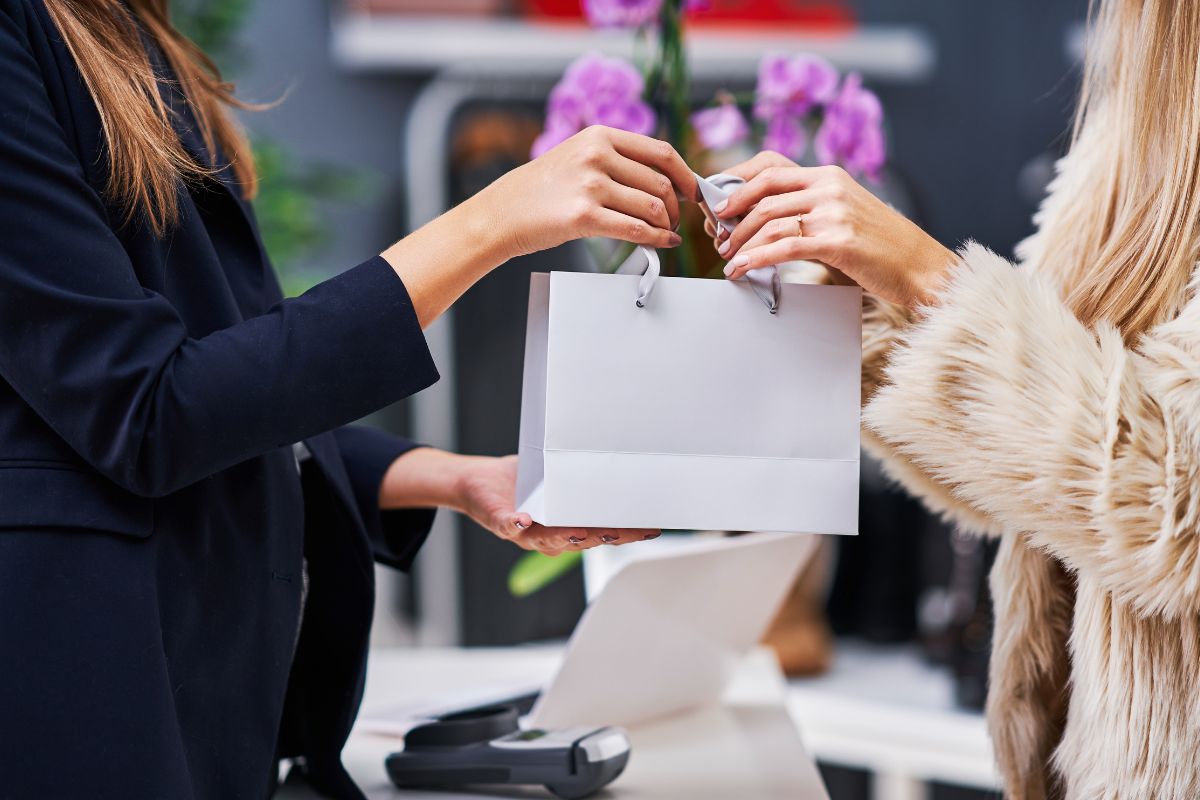 The photo shows a card swipe machine and a cashier handing the bag to the customer's hand referring to avoiding lifestyle inflation means keeping more money.