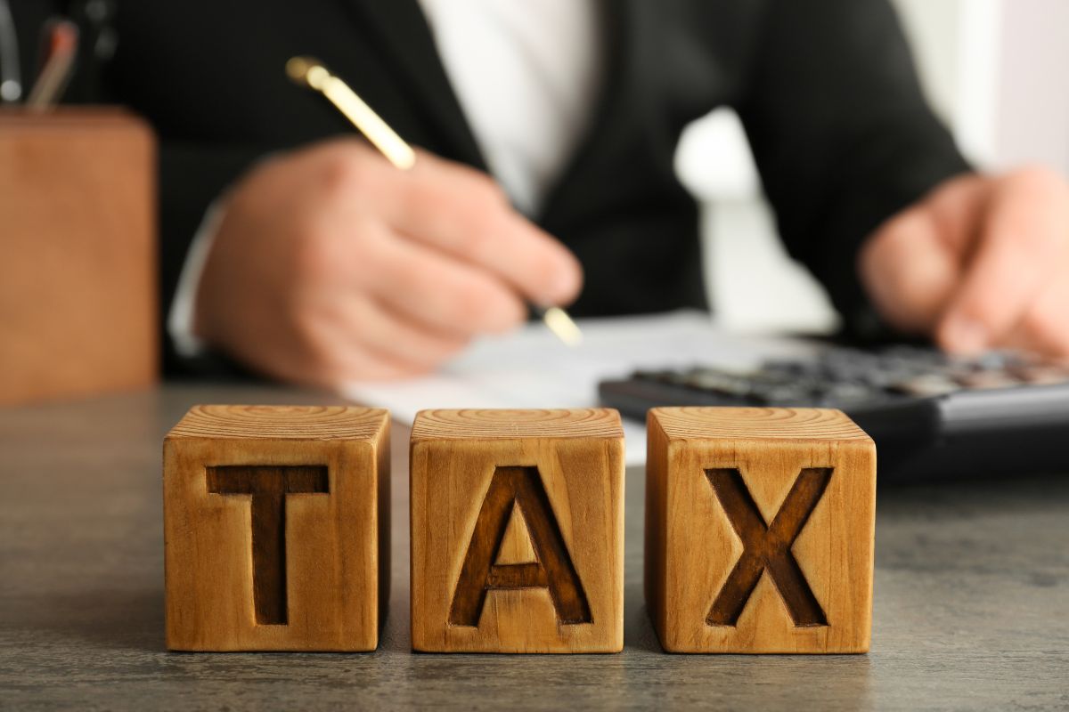 The picture shows a man writing on paper while using a calculator and wooden cubes with letters which means learning tax strategies to help you grow wealth faster.