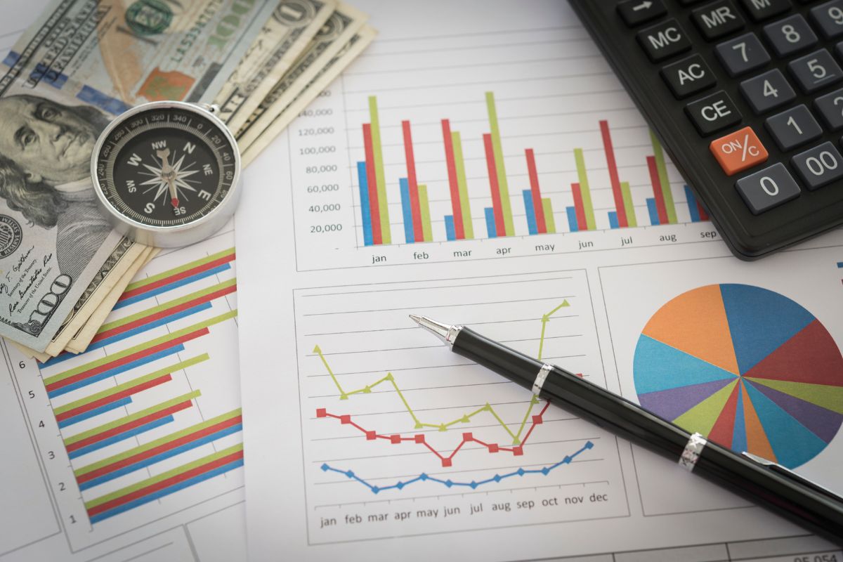 The picture shows a calculator, a compass, dollar bills, a pen, and papers with graphs which means documenting and analyzing financial progress regularly helps them make better money choices and fix mistakes fast. 