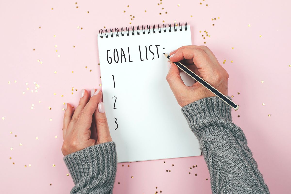 The photo of a woman's hand writing a goals list in a notebook.
