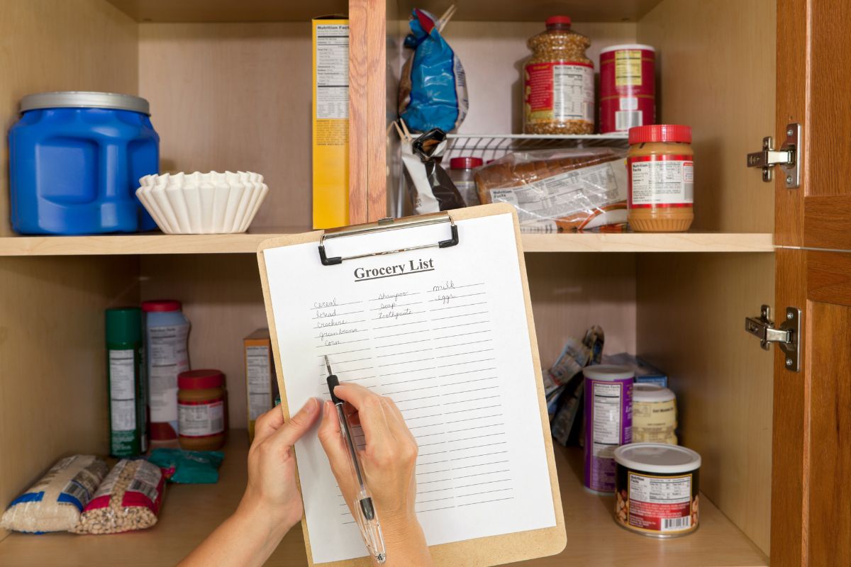The image shows a woman's hand making a grocery list.