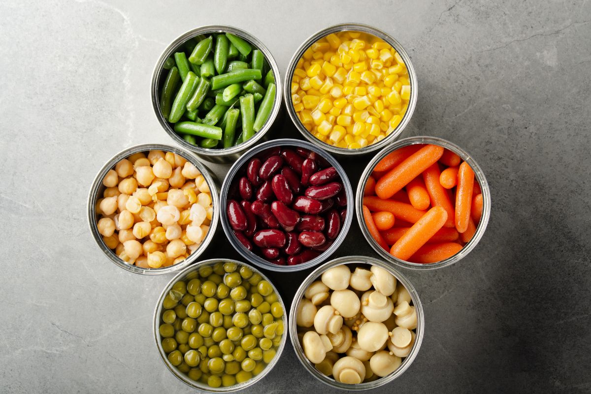 The photo shows cans with beans, sausages, corn, and mushrooms on the table which means using perishable items first prevents food from being wasted and helps you stretch your budget.