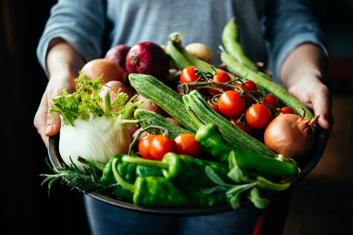 The image shows a tray of vegetables handed by a girl's hand referring to swapping ingredients with friends or neighbors keeps grocery costs low and prevents food from going to waste.