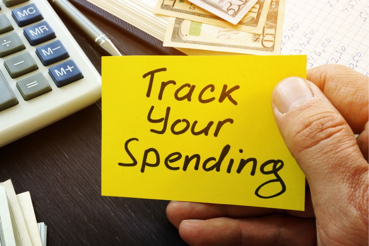 A man's hand holding a paper with Track Your Spending wording.