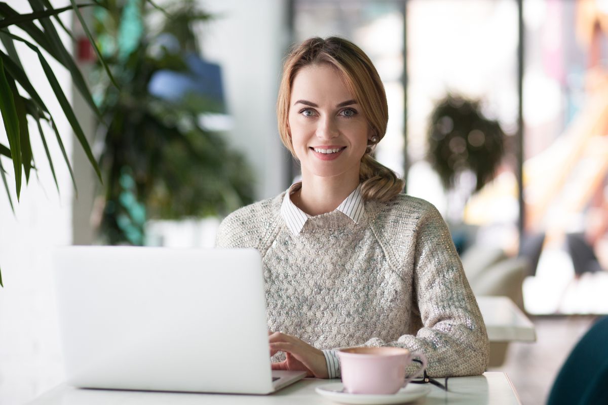 The picture shows a girl using a laptop while having a coffee indicating to get started on your no-spend challenge and the download template helps keep track of progress and savings.