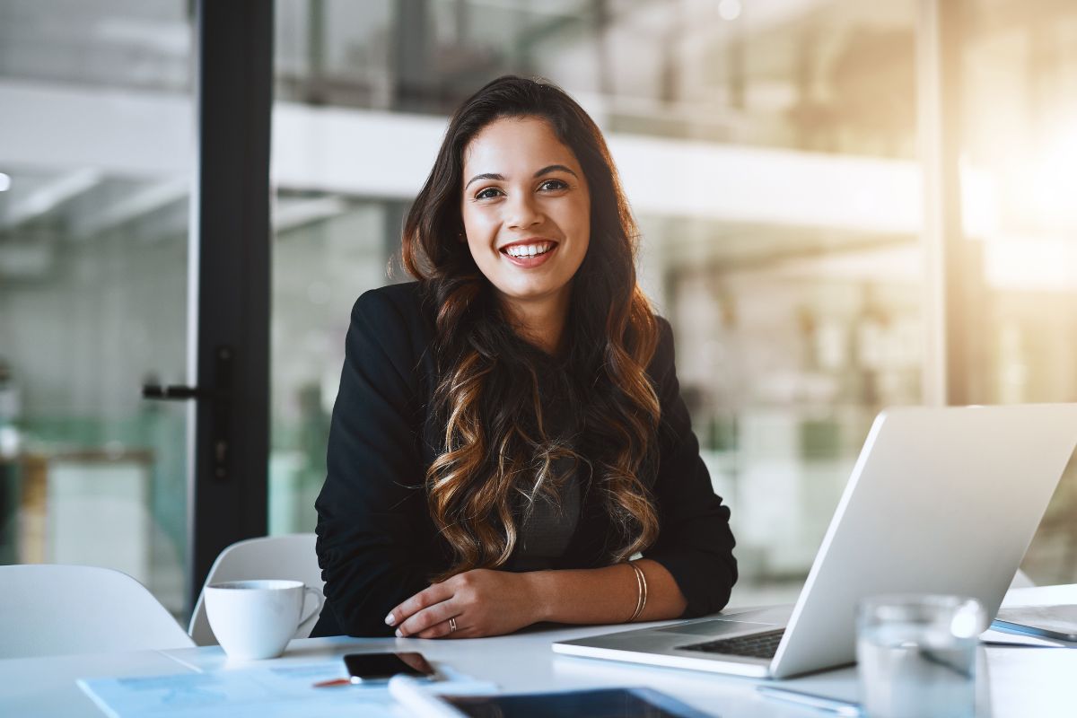 The picture shows papers on the table, a phone, a laptop, a mug, and a girl in a suit which means allowing for career switching can improve your financial future.