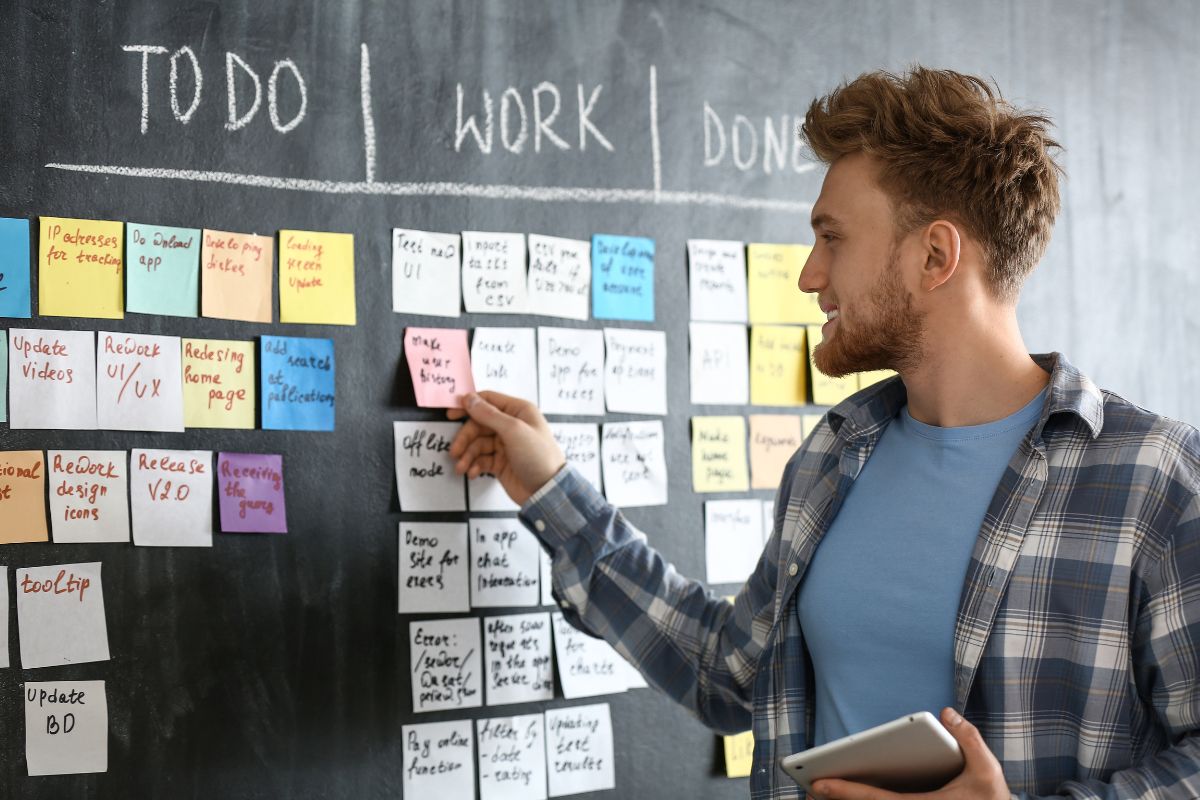 The picture shows a board with sticker notes and a man arranging them which means learning new skills provides the ability to delegate tasks means more growth and profit.