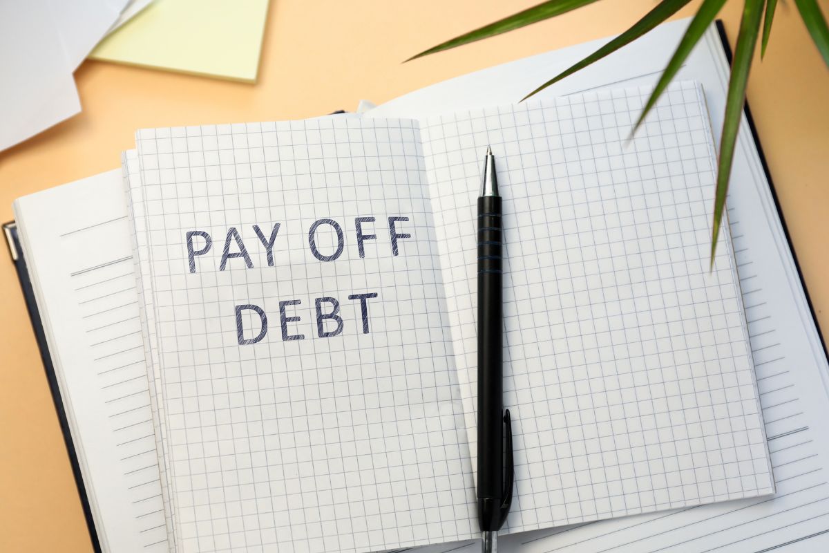 The photo of a pen and a notebook with payoff debt wording.
