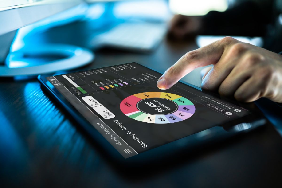The image of a man's hand using a tablet device with a screen display indicates that using a budgeting app with alerts is and easy way to stay accountable and save money.