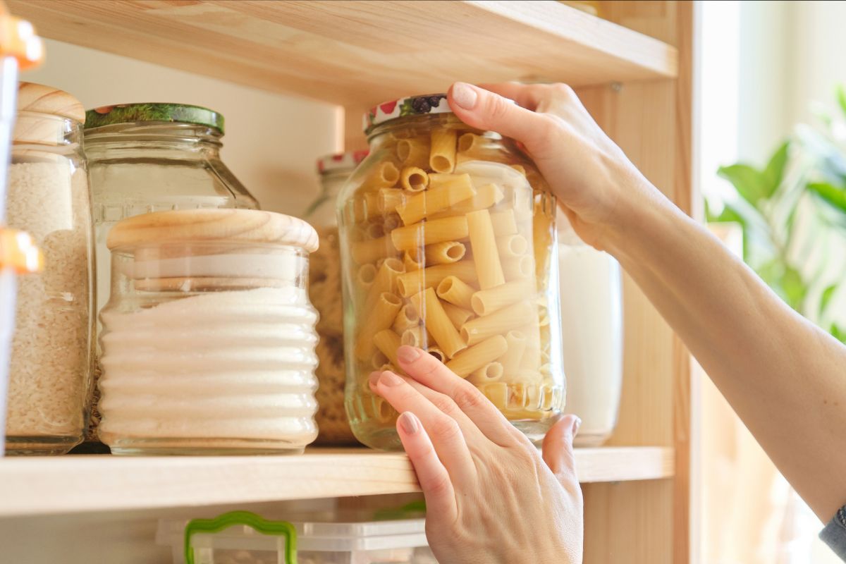 An image shows a woman getting a jar of pasta.