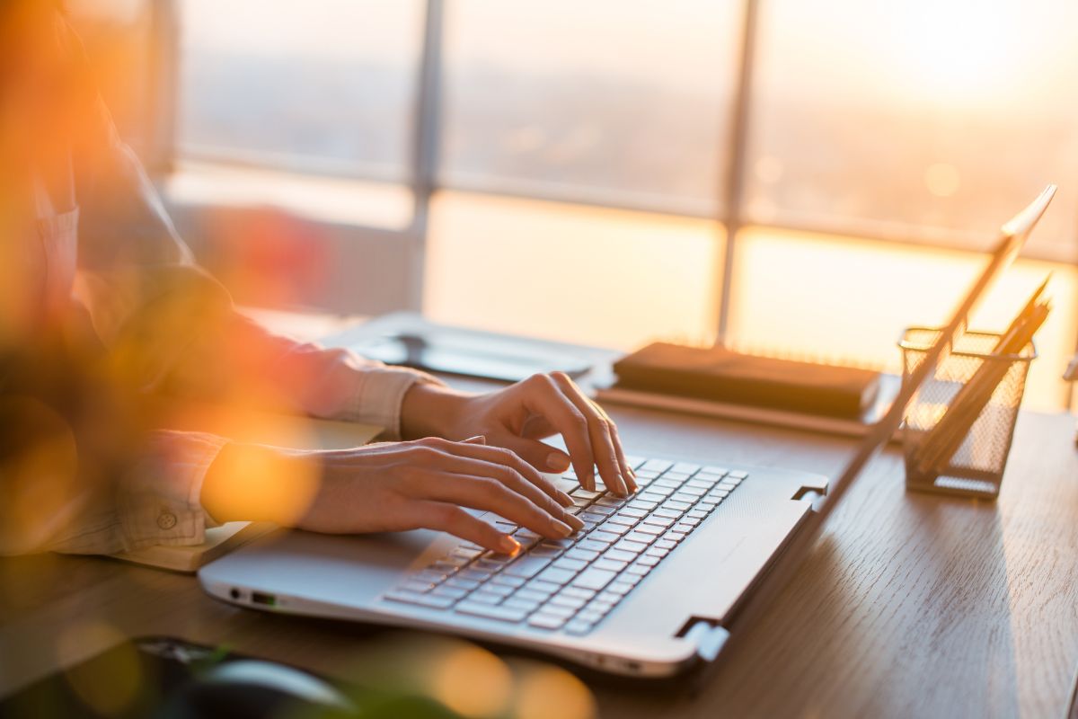 The photo shows a girl's hand typing on the laptop indicating that setting financial goals with a visual tracker helps turn savings into a habit.