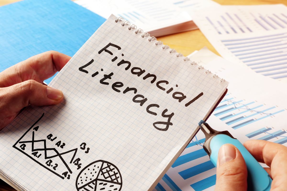 An image of a man's hand holding a notebook with financial literacy wording.