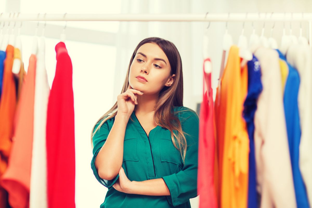 The photo of a girl looking at the clothes while thinking which means to use the one in, one out rule helps prevent overspending and keeps money in your savings.