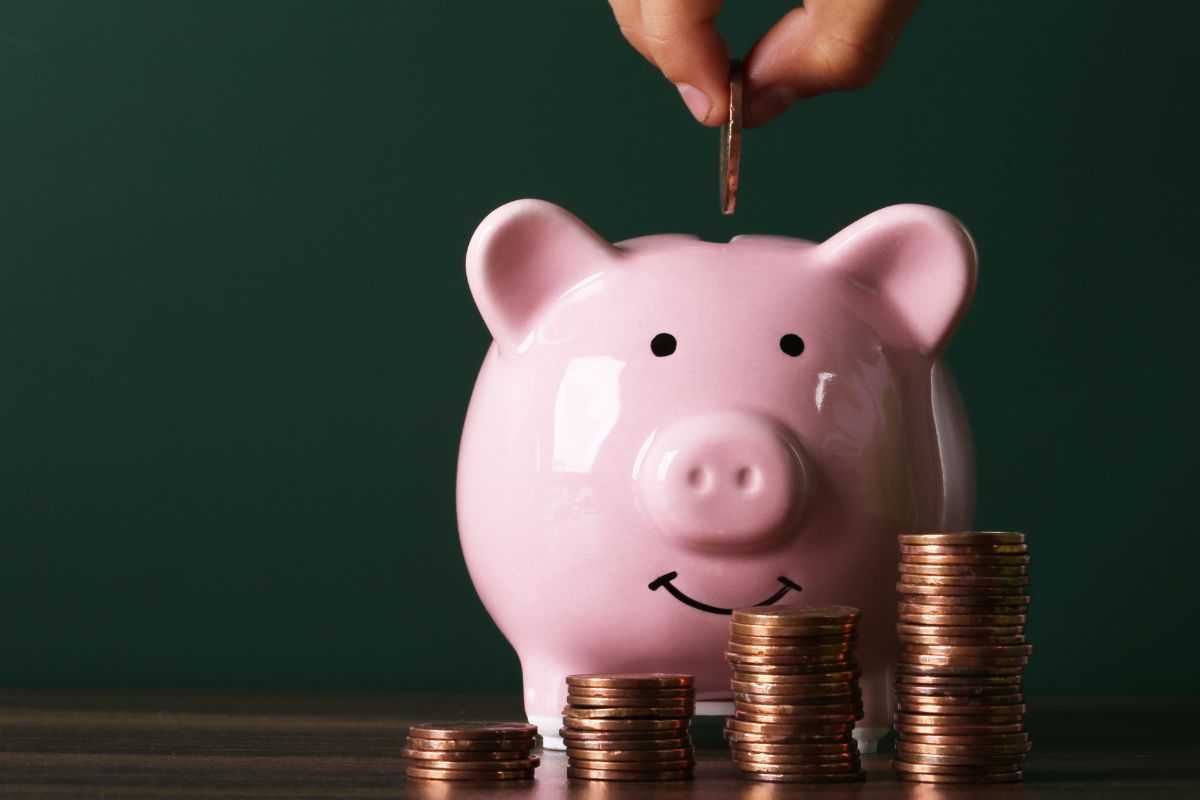 The picture shows coin stock, a piggy bank, and a man's hand dropping a coin into it indicating that turning saving into a fun challenge can help you stick to your goals.