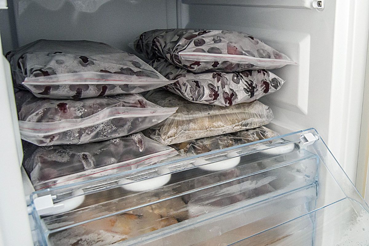 The photo shows a fridge with frozen fruits, meat, and vegetables indicating that freezing everything possible helps stretch your grocery budget by preventing waste.