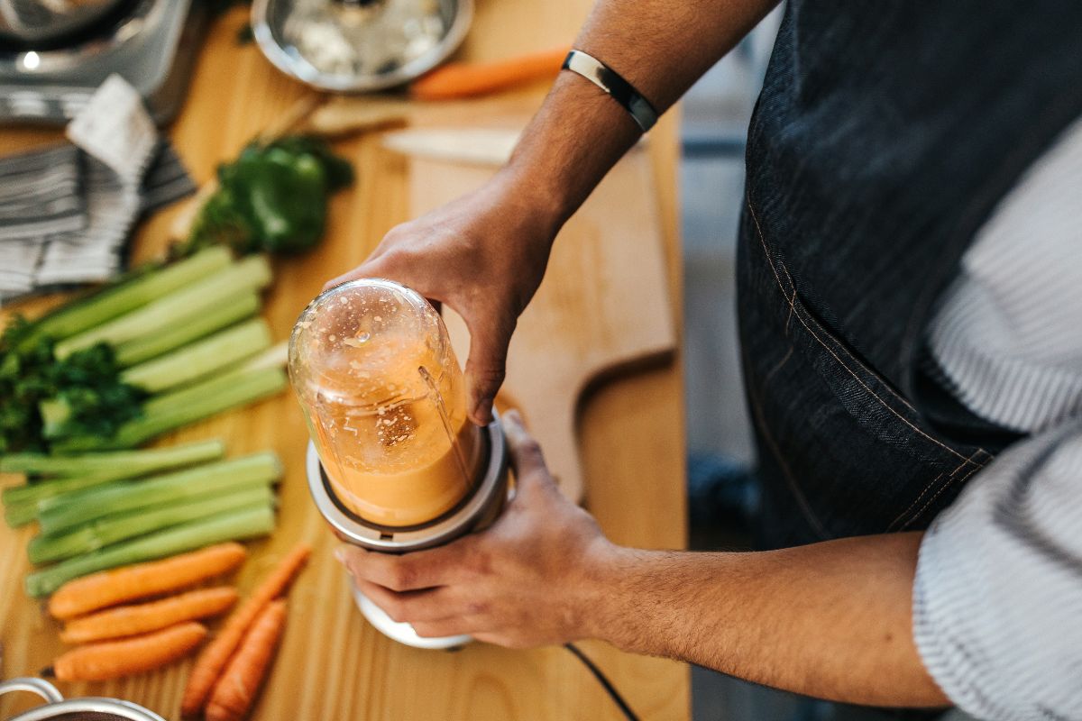 The photo shows vegetables and a man's hand using a machine which means blending veggies stems and leaves helps prevent waste and stretch food dollars.