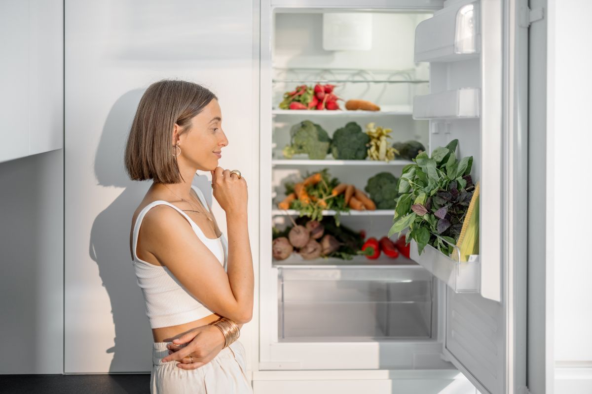 The photo of vegetables in a fridge and a girl wondering referring to plan clean-out-the-fridge meals help clear out the fridge and stretch the grocery budget.