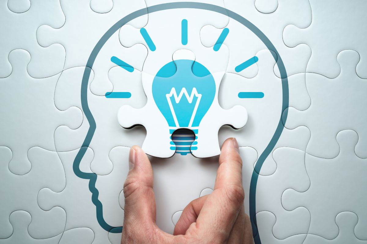 The picture tells about a man's hand holding a piece of a puzzle with a human head figure and a bulb which means learning skills increases problem-solving abilities and can lead to financial success.