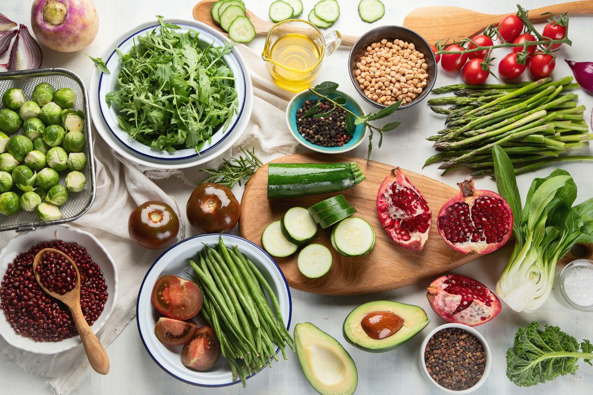 The picture shows plates with fruits and vegetables on the table, spices, beans, and more indicating that learning how to become frugal green for more savings can keep more food out of the trash and more money in your pocket.