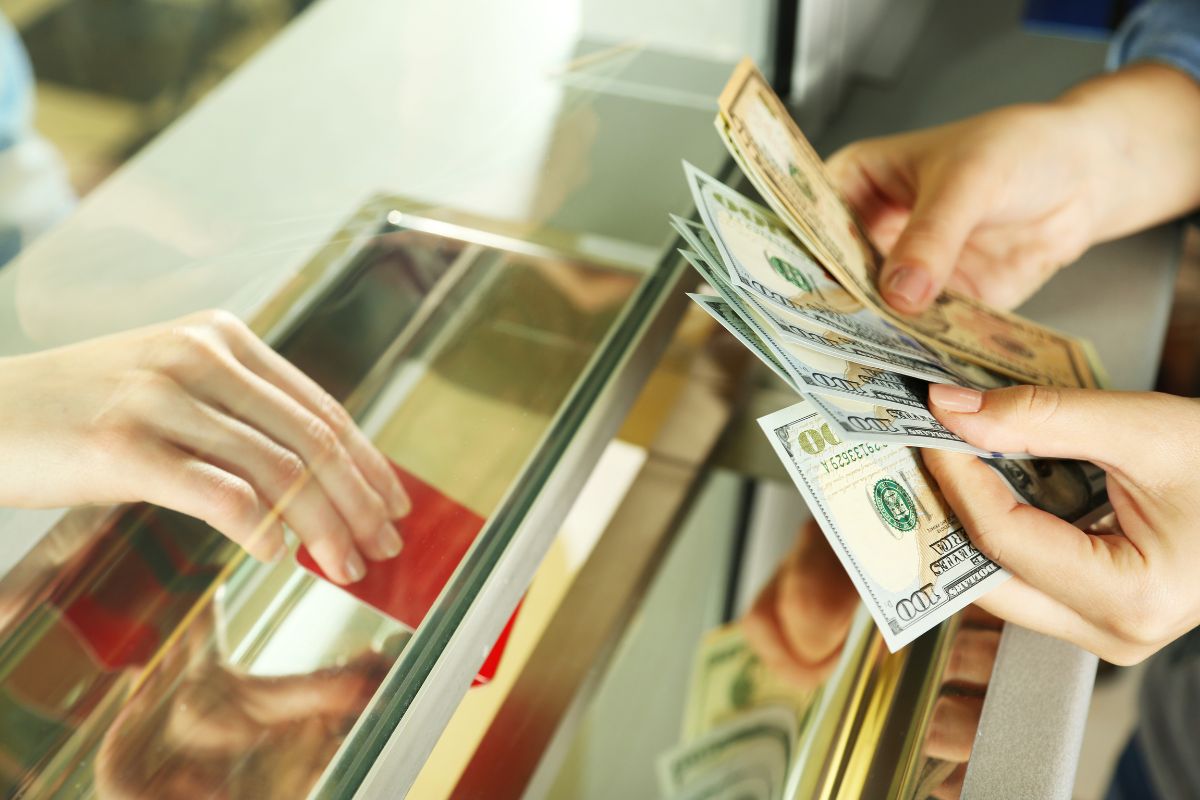 The photo shows a cashier's hand handing a red card and a customer's hand counting dollar bills which refers to using cash-only spending to help stop impulse purchases since you can't just swipe a card.