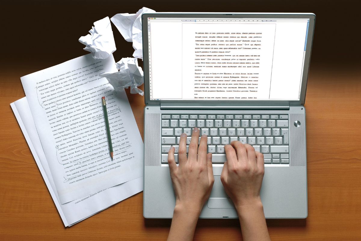 The picture shows papers, crumpled papers, a pen, and a girl's hand typing on the laptop which means learning skills enables participation in the gig economy and gives you financial stability and more options.
