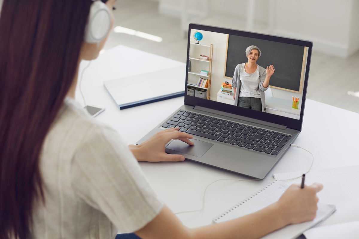 The photo shows a girl writing while listening to the teacher in her laptop referring to finding free entertainment to save money and put straight in the savings.