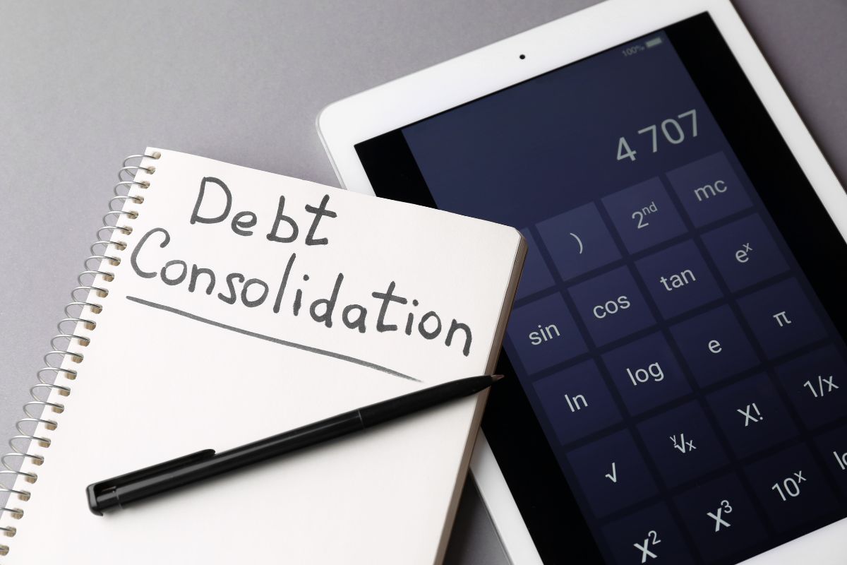 The photo shows a tablet device with a calculator, a pen, and a notebook with notes referring to how refinancing or consolidating debt helps reduce debt and frees up money each month.