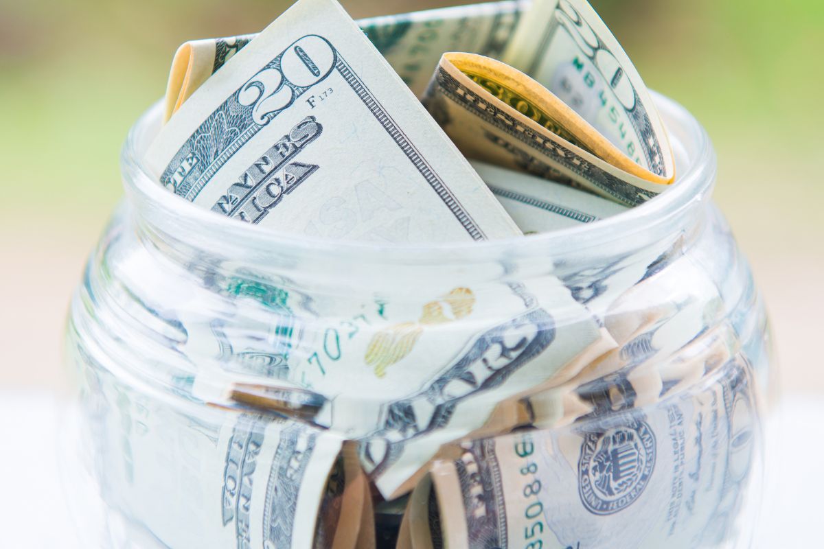 The image tells about a jar filled with dollar bills referring to saving all unexpected money to reach savings goals faster.