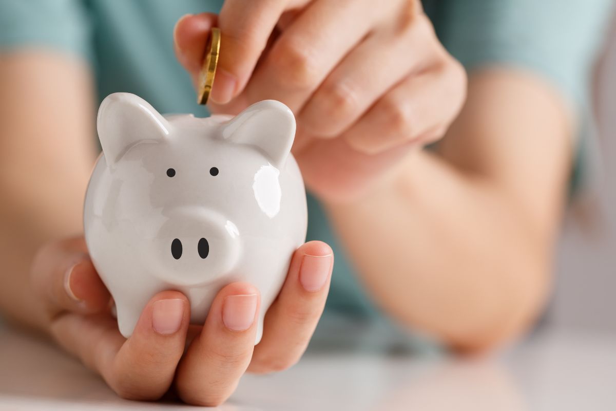 The image shows a girl's hand dropping a coin in the small piggy bank referring to turn savings into a game that keeps it fun and helps you stay motivated.