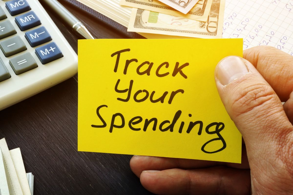 The image of a man's hand holding a paper with track your spending.
