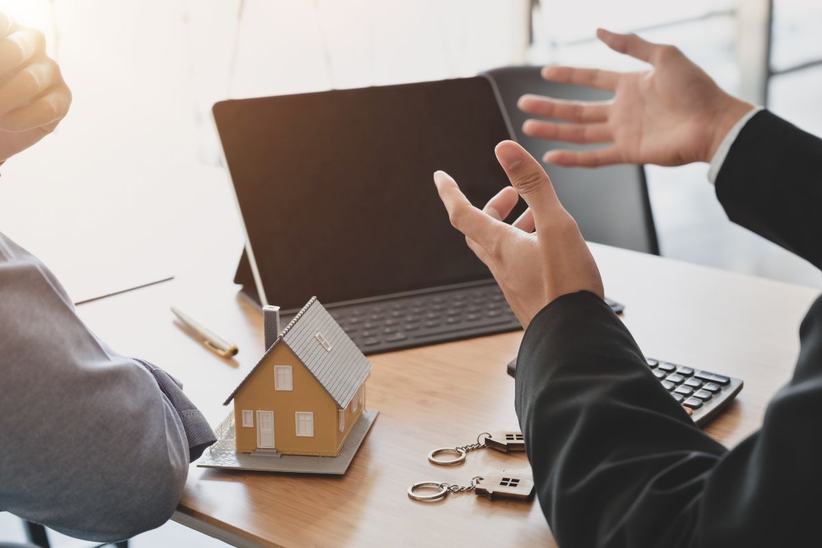 The picture shows a tablet with a keyboard, mini house keys, a calculator, and two men talking which means that negotiating everything frees up money for savings and investments.