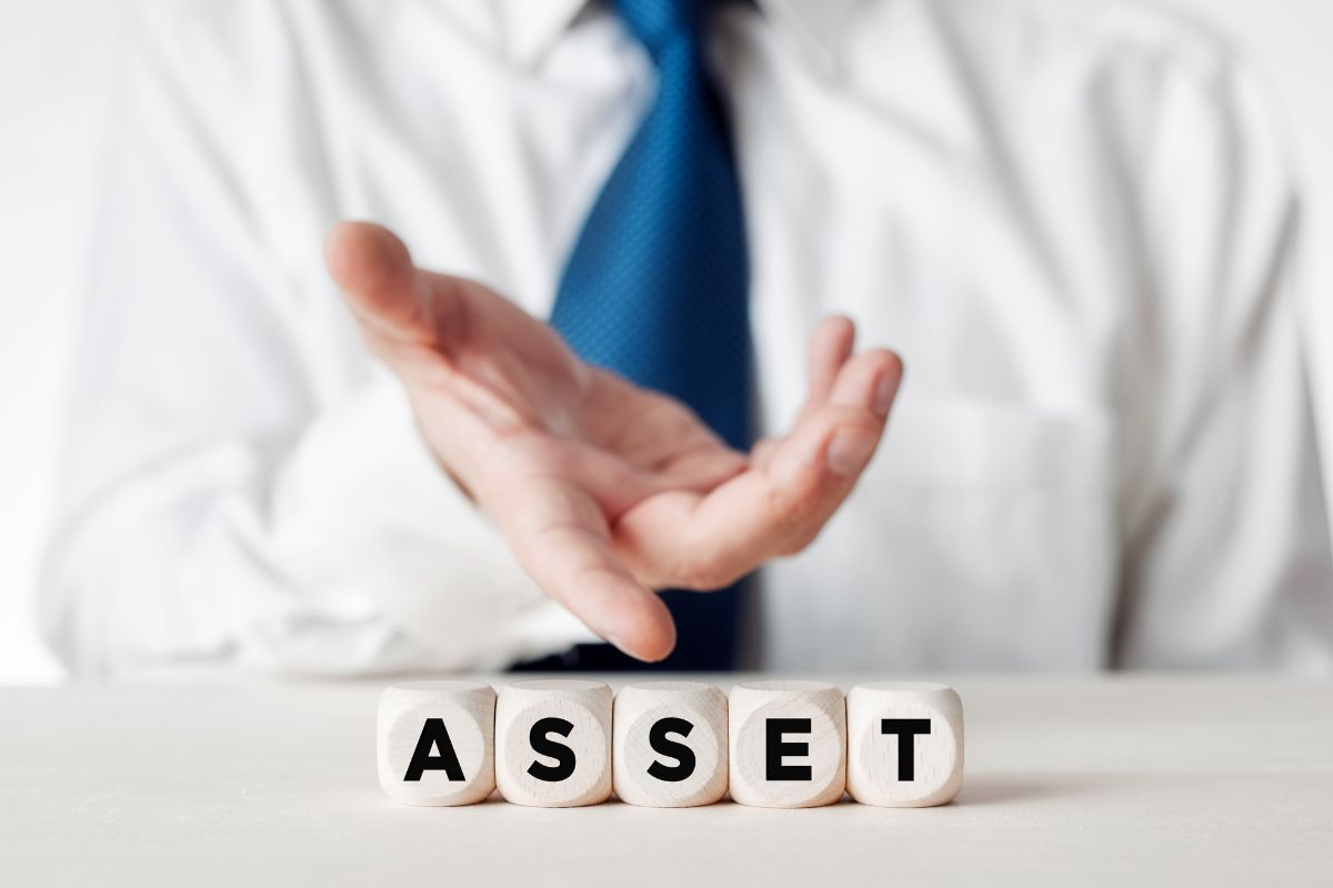 The photo shows a man in a suit pointing to the wooden cubes with letters that refer to owning assets, not liabilities building financial security.