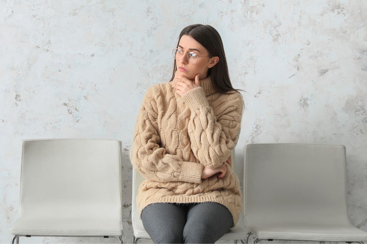 The image shows a girl thinking while waiting indicating to delay gratification builds wealth faster than quick spending.