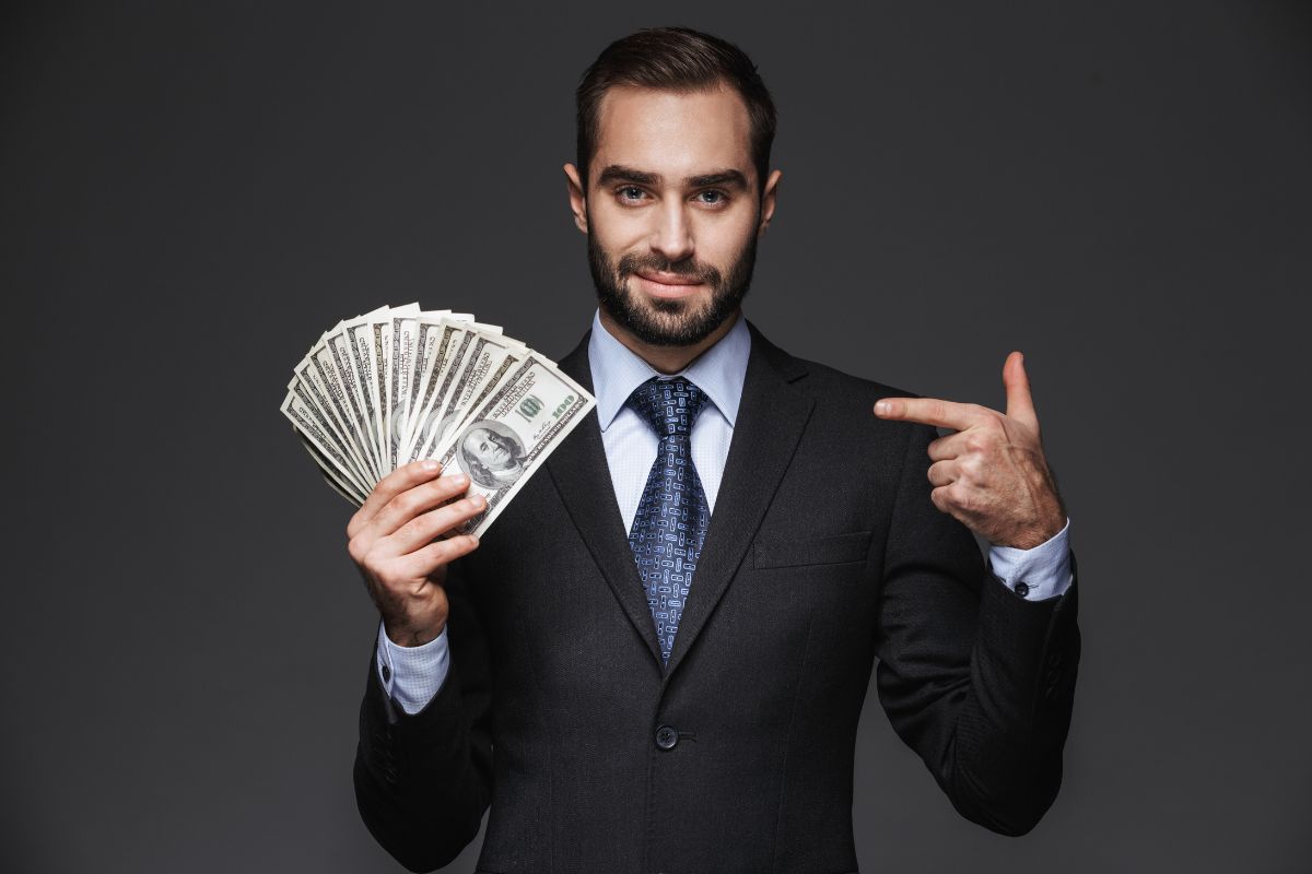 The photo shows a man holding dollar bills while pointing it which refers to leverage other people's money can build faster than saving alone.
