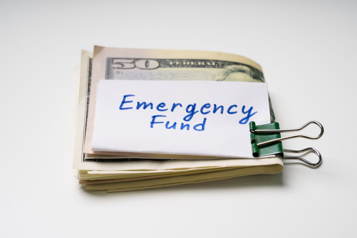 The photo shows dollar bills, a piece of paper with notes, and a clip referring to keep emergency cash reserves provide security and pece of mind.