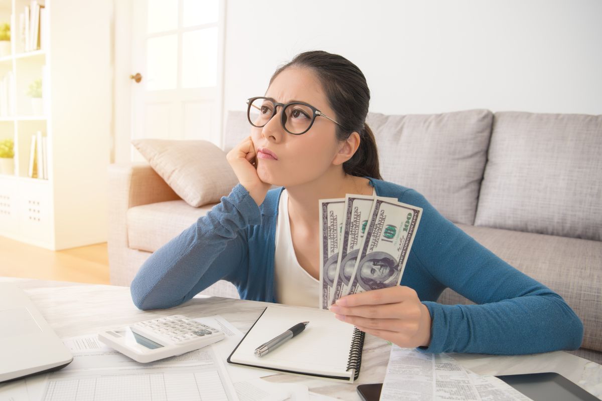 The mage shows a calculator, a notebook with a pen, and a girl holding dollar bills while thinking referring to the plan for big expenses keeps your finances under control and less stressful.