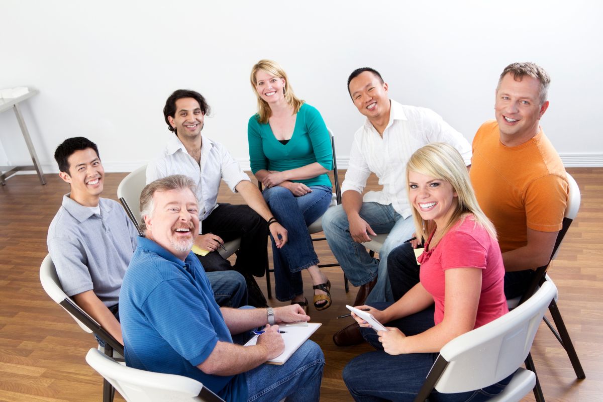 The image shows a group of people forming a circle and smiling which means to surround yourself with financially savvy people encourages smarter investing and spending.
