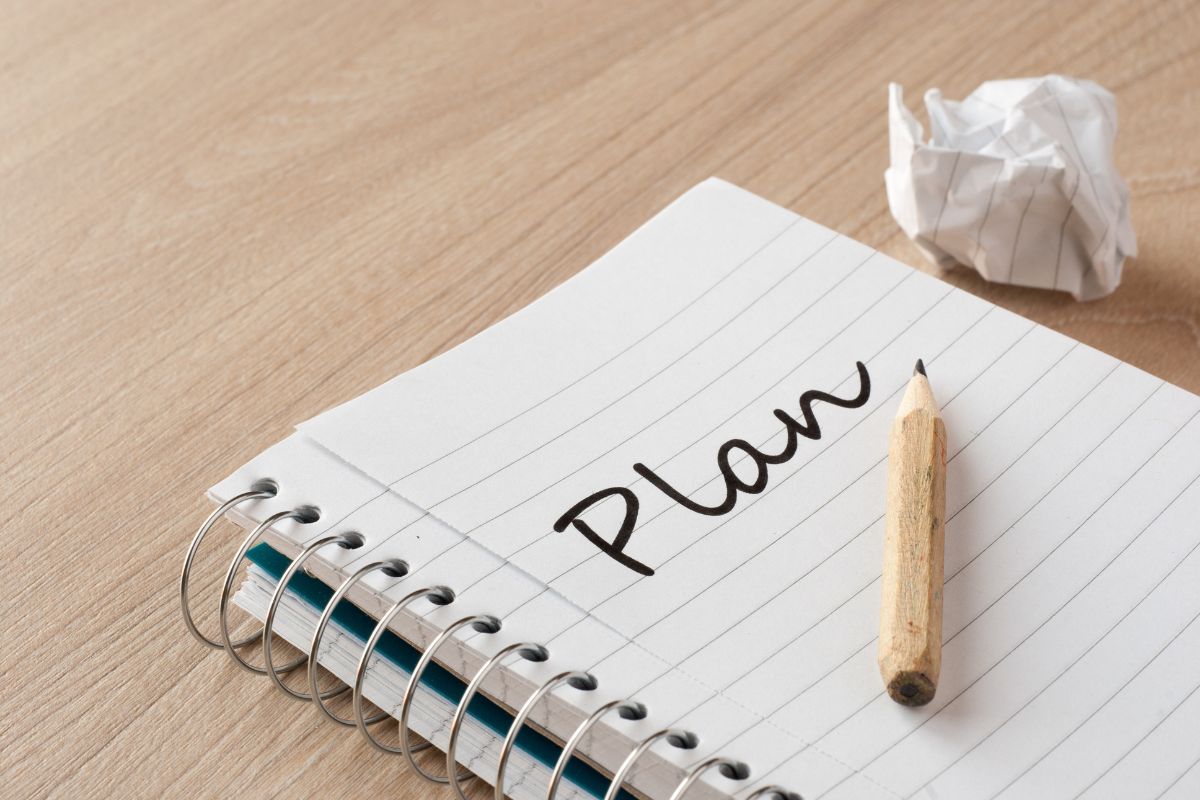 The photo shows a crumpled paper, a pen, and a notebook with a note which refers to creating a financial freedom plan that makes saving and investing easier.