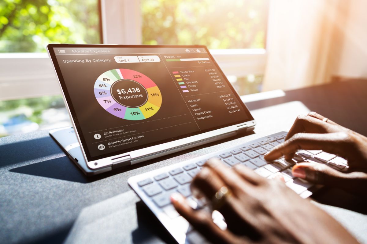 The photo shows a girl's hand using a laptop with a screen display indicating that using budgeting apps helps organize expenses and track spending.