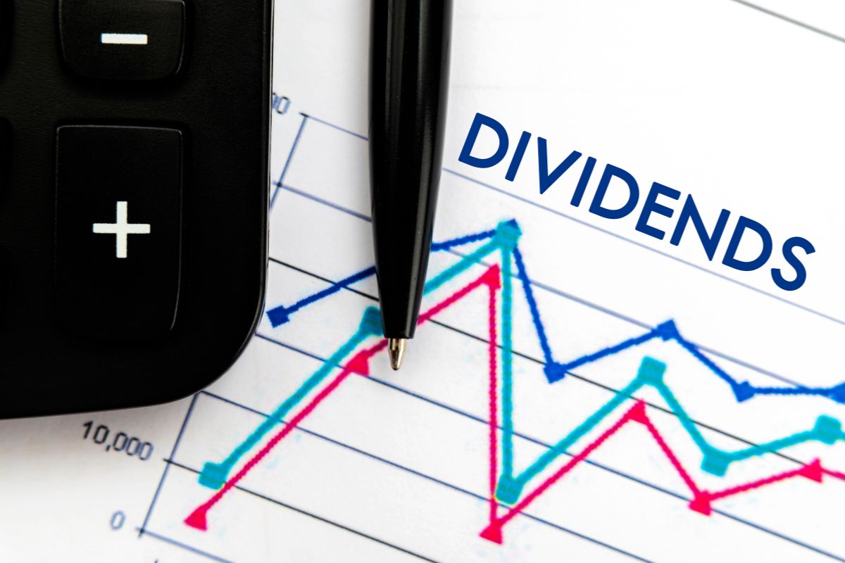 The photo shows a calculator, a pen, and a piece of paper with a graph, numbers, and notes which means investing in dividend stocks is a hands-off way to make money online while you sleep.