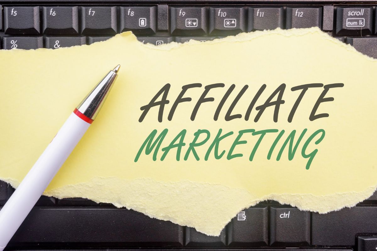 The photo shows a keyboard, a pen, and a piece of paper with notes referring to how starting an automated affiliate website can grow into a steady source of income.