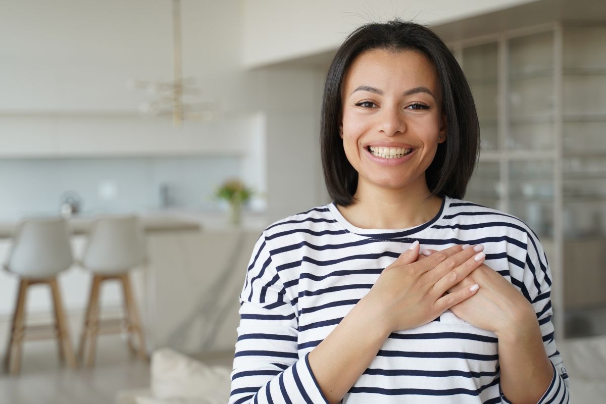 The image shows a girl placing both hands on her chest indicating that expressing appreciation for current wealth keeps you from feeling stuck and opens your mind to better financial opportunities.