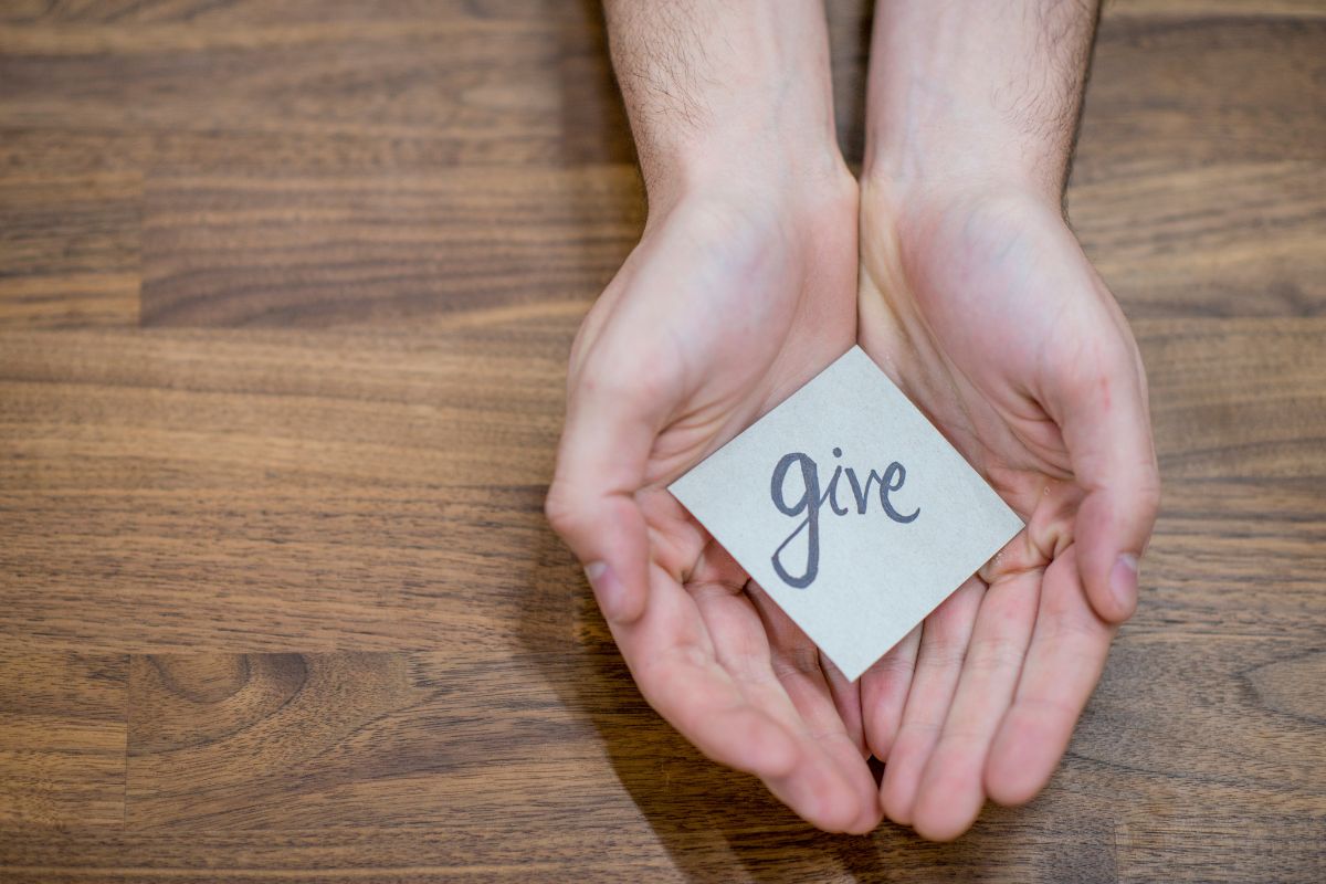 The photo tells about a man's hand holding a piece of paper with a note indicating showing generosity and giving without expectation strengthens connections and brings unexpected financial opportunities.