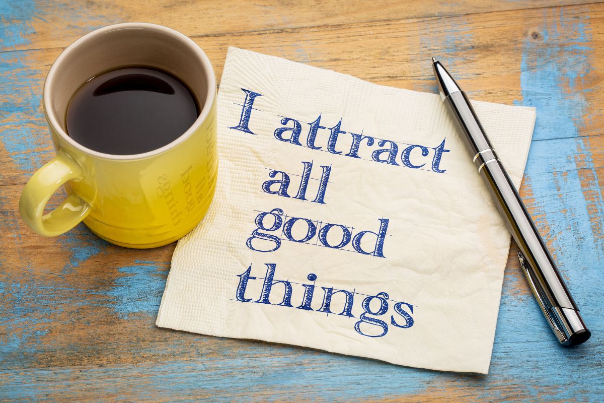 The picture shows a pen, a coffee, and a piece of paper with notes which means to use affirmations to reinforce financial gratitude.