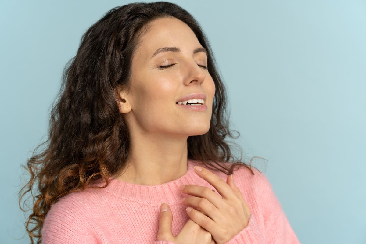 The image shows a girl putting her hands on her chest referring to being thankful for opportunities to earn and invest helps you take action instead of feeling stuck.