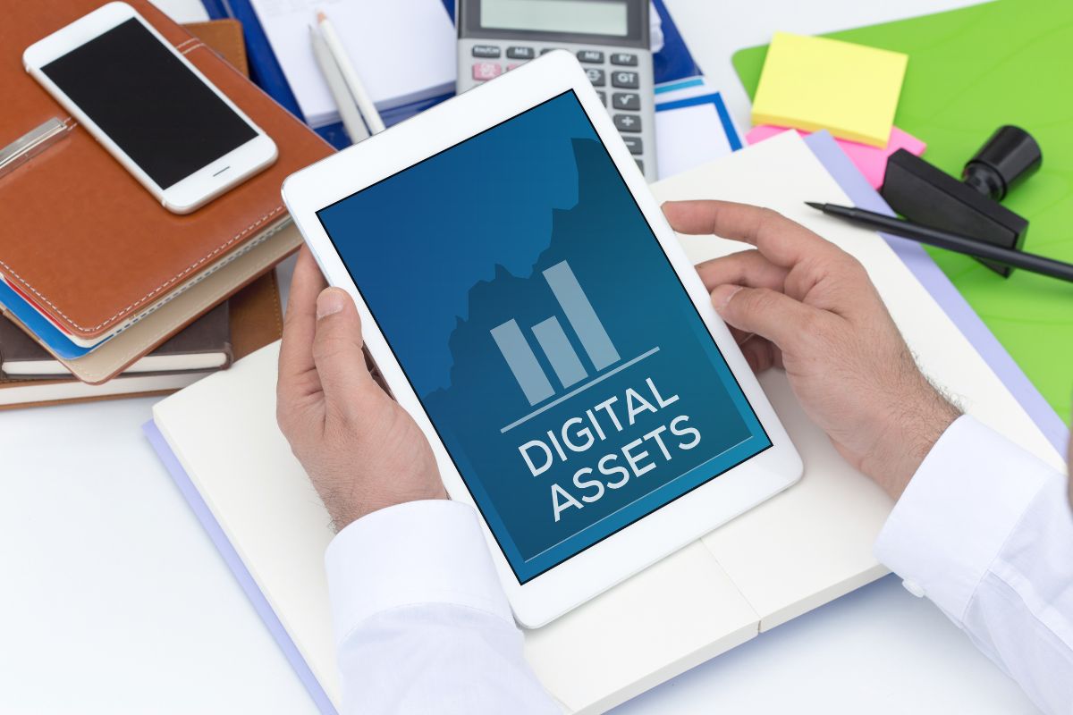 The image shows notebooks, a calculator, sticker notes, and a man's hand holding a tablet device with a screen display which means that renting out digital assets is an easy way to make passive income online.